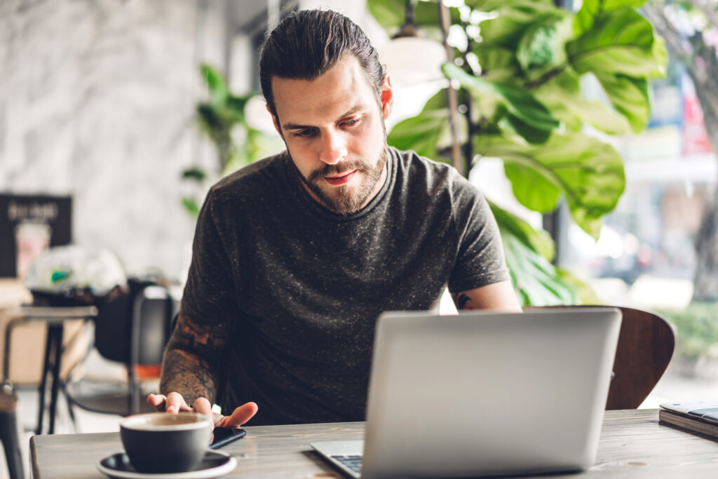 Handsome bearded hipster man use and looking at laptop computer with coffee at table in cafe.Communication and technology concept