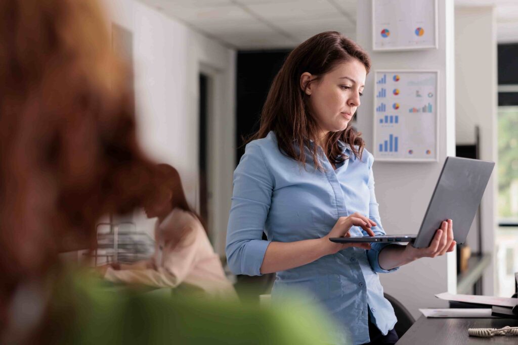 A worker in a company stands accessing a business system via a laptop in an office.