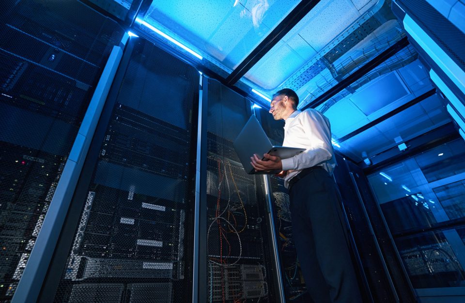 Server administrator of data center with laptop in one hand checking network cabinet