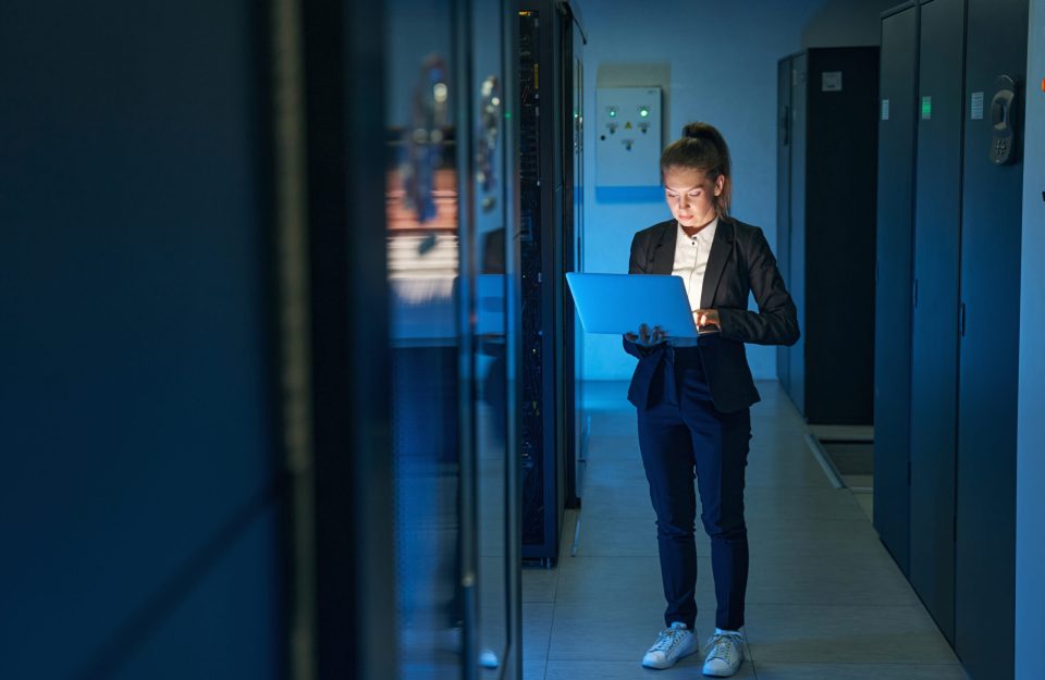 Young woman IT engineer use laptop computer while working with supercomputer in data center server room