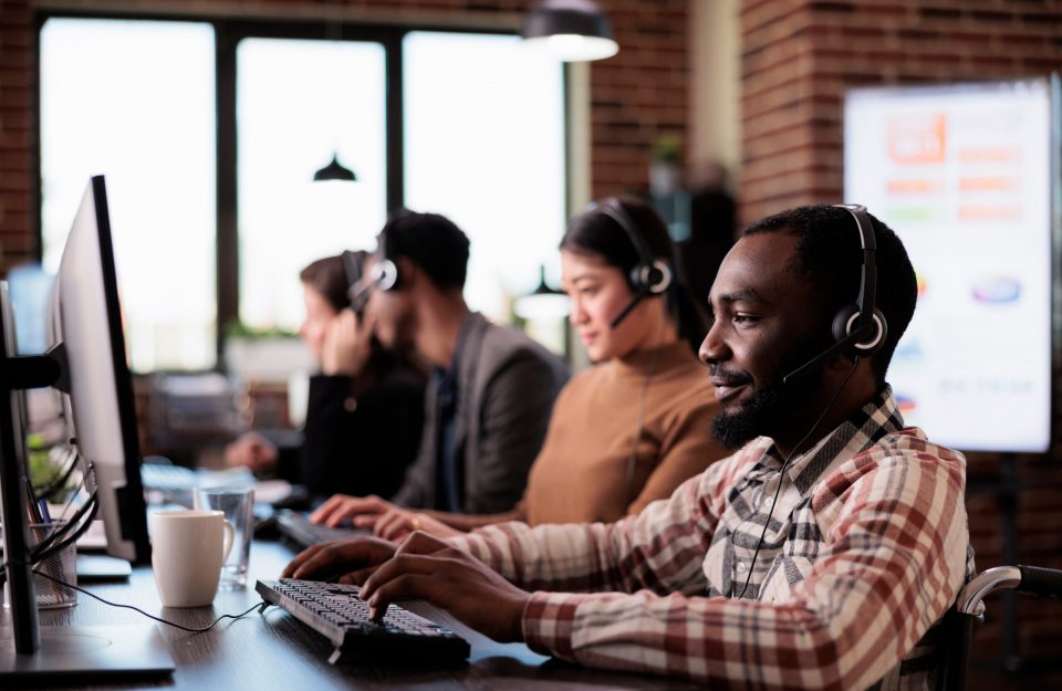 Customer service employee with chronic health condition working at call center helpdesk. Male client care operator with impairment sitting in wheelchair in disability friendly office.