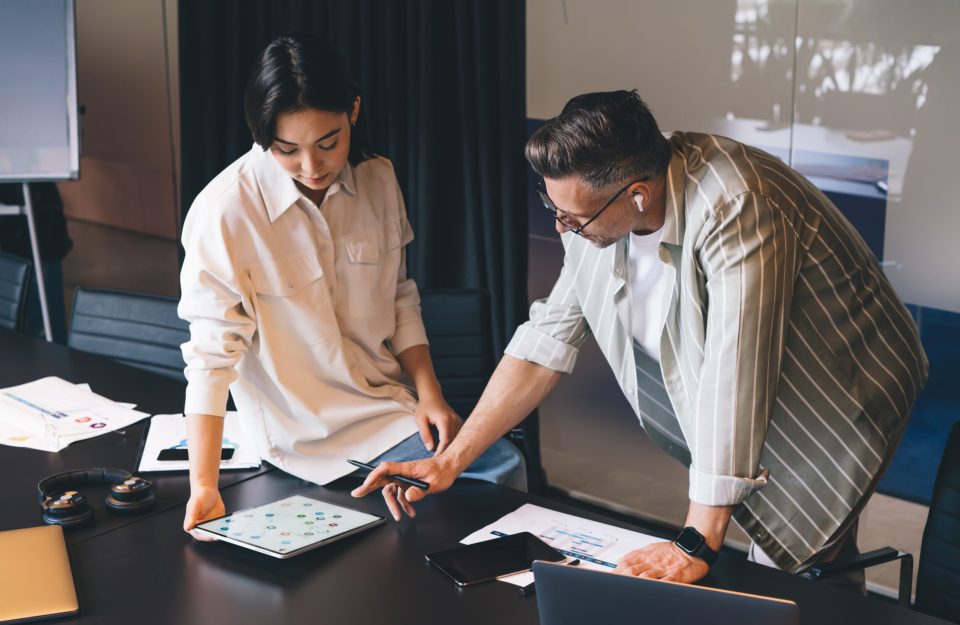 Diverse entrepreneurs in earbuds working together on UI UX graphic design for product connecting to wg wireless on digital tablet, smart casual employees browsing analytic on modern touch pad