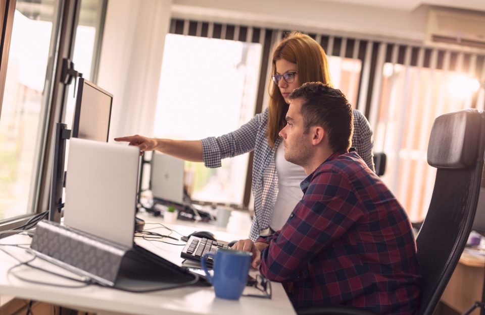 Two software developers working on a new project in a software developing company office. Focus on the woman poiting to the comuter screen